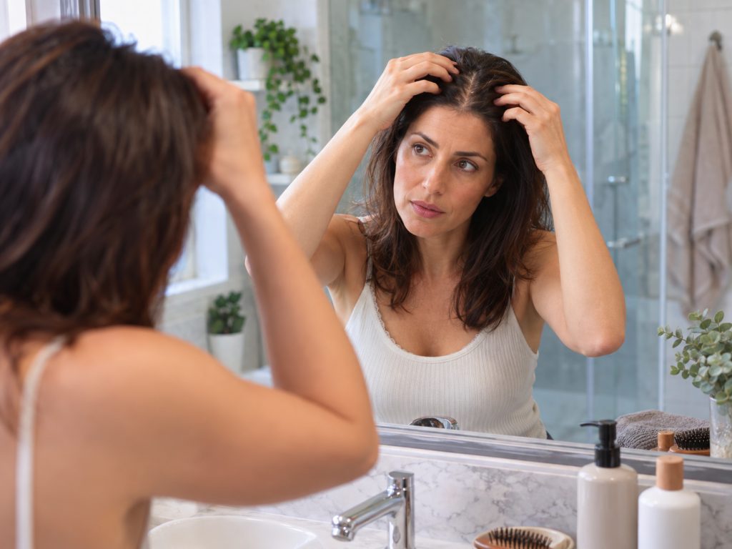 Donna che controlla il diradamento dei capelli allo specchio durante la routine per alopecia androgenetica femminile